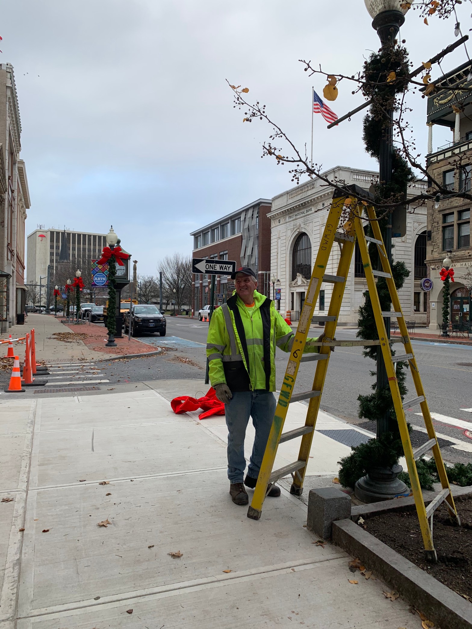Man with ladder hanging garland on street light